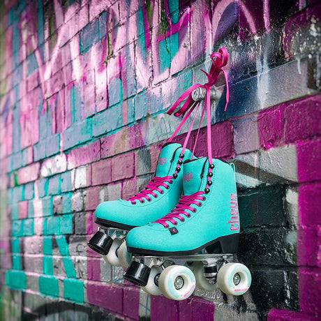 Turquoise roller skates with pink laces hanging on a colorful brick wall.